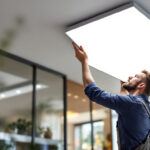 A photograph of a lighting contractor installing or inspecting a sleek led ceiling panel in a modern interior space