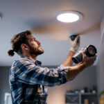 A photograph of a lighting contractor installing 2-inch led recessed lights in a modern ceiling