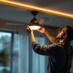 A photograph of a skilled lighting contractor installing or adjusting a modern ceiling fan with integrated smart lighting features in a stylish living space