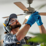 A photograph of a skilled lighting contractor carefully replacing a ceiling fan light cover