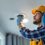 A photograph of a lighting contractor installing a recessed electrical outlet in a ceiling
