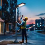 A photograph of a solar lamppost illuminating a modern urban street at dusk