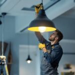 A photograph of a skilled lighting contractor installing a stylish hanging lamp in a modern interior space