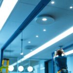 A photograph of a lighting contractor installing commercial recessed can lights in a modern office space