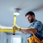 A photograph of a lighting contractor measuring and installing recessed lighting fixtures in a modern home