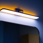 A photograph of a stylishly designed offset vanity light installed above a contemporary bathroom mirror