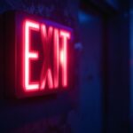 A photograph of a glowing incandescent exit sign in a dimly lit environment