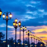 A photograph of a well-lit urban street scene featuring a variety of lamp post poles at dusk