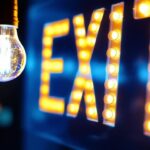 A photograph of a close-up view of an illuminated exit sign with a focus on the light bulb
