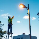 A photograph of a lighting contractor installing a 20-foot light pole in an urban or commercial setting