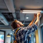 A photograph of a lighting contractor installing a sleek drop ceiling light fixture in a modern commercial space