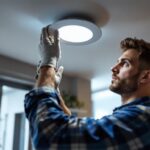 A photograph of a lighting contractor installing a 6-inch recessed led retrofit in a modern home setting