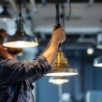 A photograph of a skilled lighting contractor installing sleek metal hanging lights in a modern workspace