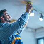 A photograph of a skilled lighting contractor installing or adjusting track lighting in a modern interior space