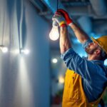 A photograph of a lighting contractor installing high lumen light bulbs in a modern workspace