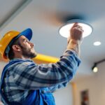 A photograph of a lighting contractor expertly installing a wafer light bracket in a modern ceiling