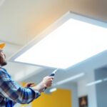 A photograph of a lighting contractor installing a 2x4 led panel in a commercial space