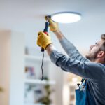 A photograph of a lighting contractor carefully replacing a recessed can light with an led fixture