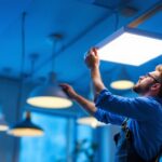 A photograph of a skilled lighting contractor installing or adjusting flat panel lights in a modern interior space