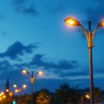 A photograph of a well-lit street scene featuring modern pole street lights illuminating a bustling urban environment at dusk