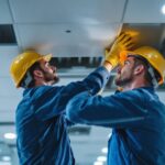 A photograph of a lighting contractor installing recessed drop ceiling tiles in a commercial space