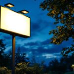 A photograph of a well-lit outdoor sign illuminated by solar lights at dusk