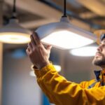 A photograph of a lighting contractor installing or testing modern indoor emergency lights in a commercial setting