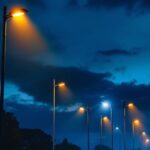 A photograph of a well-lit street scene featuring various styles of street lighting poles