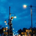 A photograph of a well-lit urban street scene featuring various light poles