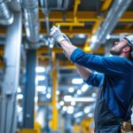 A photograph of a lighting contractor actively engaged in installing or adjusting energy-efficient lighting systems in a commercial or industrial setting