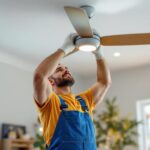 A photograph of a skilled lighting contractor installing a modern ceiling fan in a stylish home interior