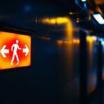 A photograph of a well-lit emergency exit sign in a dimly lit corridor