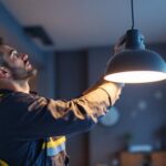 A photograph of a lighting contractor expertly installing or adjusting a stylish satco light fixture in a modern interior space