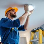 A photograph of a skilled lighting contractor installing can lights in a drop ceiling