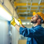 A photograph of a skilled lighting contractor installing or servicing an 8-foot fluorescent light fixture