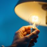 A photograph of a close-up of a hand installing a led light bulb into a modern lamp
