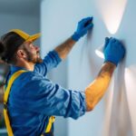 A photograph of a skilled lighting contractor installing a wall light fixture in a stylish interior setting