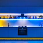 A photograph of a beautifully illuminated kitchen featuring vibrant led strip lighting under cabinets and along shelves