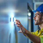 A photograph of a lighting contractor inspecting or installing a wall occupancy sensor in a modern commercial space