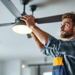 A photograph of a skilled lighting contractor installing or adjusting a stylish ceiling fan in a modern living space