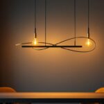 A photograph of a stylish black and brass linear chandelier elegantly illuminated in a modern interior setting